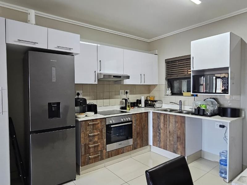 Modern kitchen featuring two-tone cabinetry, built-in oven and hob, extractor fan, and tiled flooring with a functional layout.