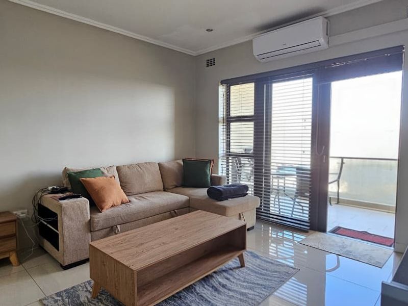 A bright living room featuring tiled flooring, a wall-mounted air conditioning unit, and a sliding glass door providing access to a balcony.