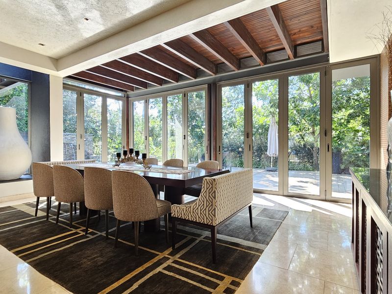 Elegant dining room featuring exposed timber ceiling beams, polished tile flooring, and expansive aluminium stacking doors providing seamless access to the garden.