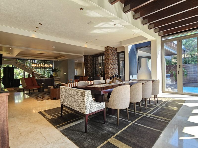 Spacious open-plan living and dining area featuring stone flooring, exposed timber ceiling beams, and large glass doors opening to the pool area.