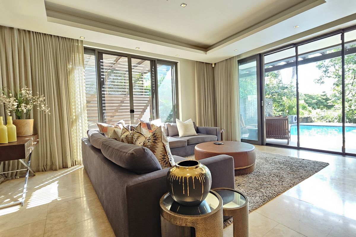 Spacious living room featuring high-quality stone flooring, recessed ceiling lighting, and large sliding glass doors providing seamless access to the outdoor pool area.