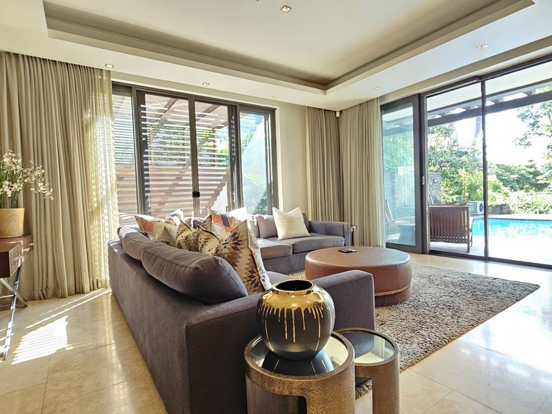 Spacious living room featuring high-quality stone flooring, recessed ceiling lighting, and large sliding glass doors providing seamless access to the outdoor pool area.