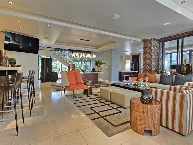 Spacious open-plan living area featuring stone flooring, recessed lighting, a built-in bar, and a modern staircase with a glass balustrade.