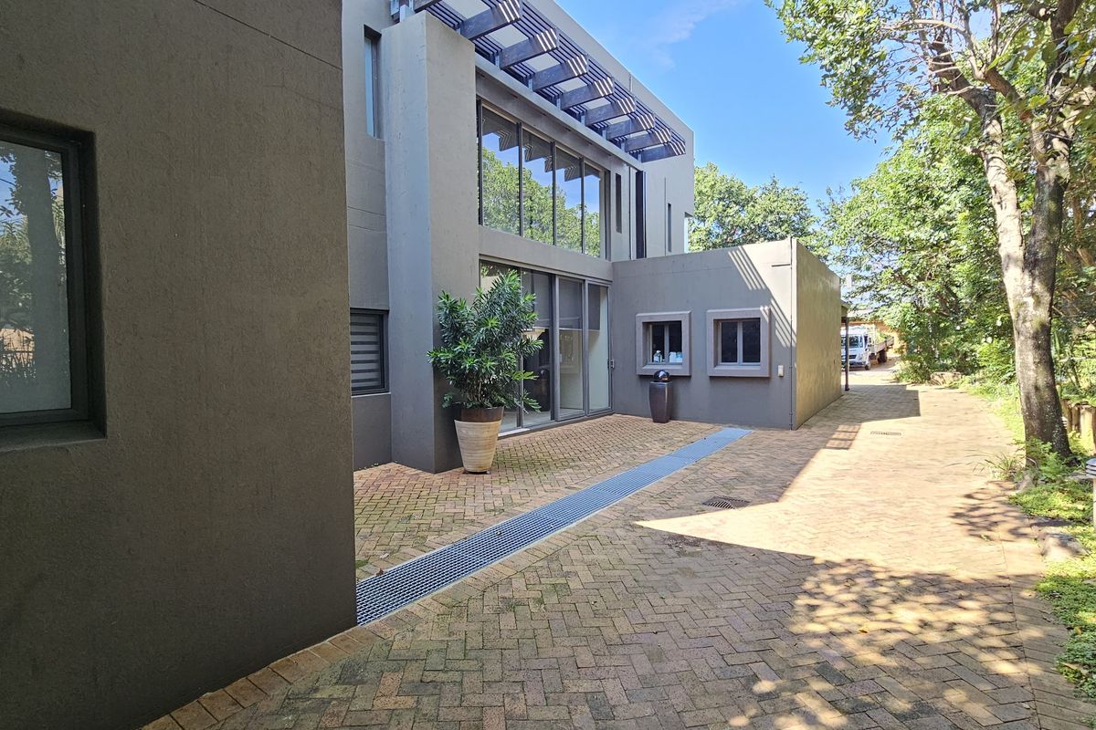 Rear exterior view of a modern home featuring paved courtyard, large glass sliding doors, and architectural pergola detail.