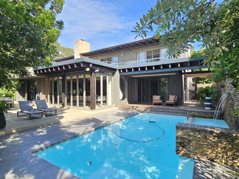 A well-maintained outdoor entertainment area featuring a swimming pool with a stone water feature, timber decking, and a covered patio with stacking glass doors.