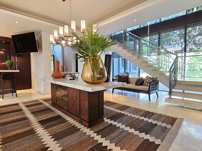 Spacious open-plan living area featuring high-end marble flooring, a striking floating staircase with glass balustrades, and a modern kitchen with built-in cabinetry.