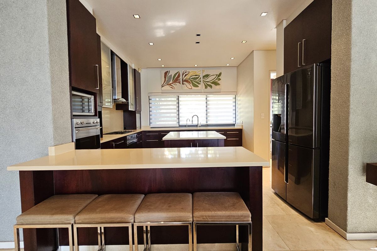 Modern kitchen featuring dark wood cabinetry, stone countertops, a central island, and integrated appliances with recessed lighting throughout.