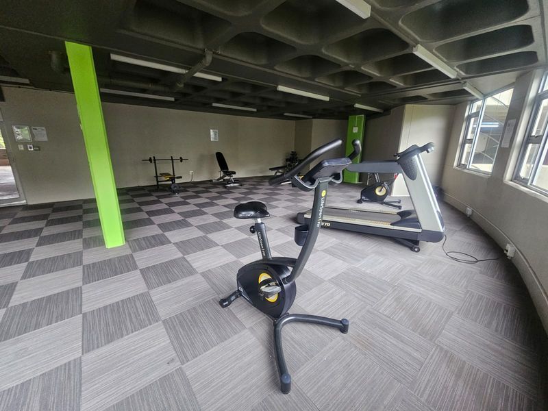 A functional apartment gym space featuring a waffle slab ceiling, carpet tile flooring, and large windows providing natural light.