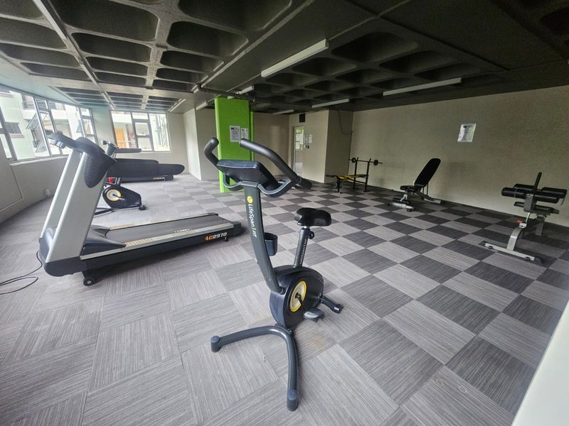 A functional apartment complex gym featuring a waffle slab ceiling, carpet tile flooring, and large windows providing natural light.
