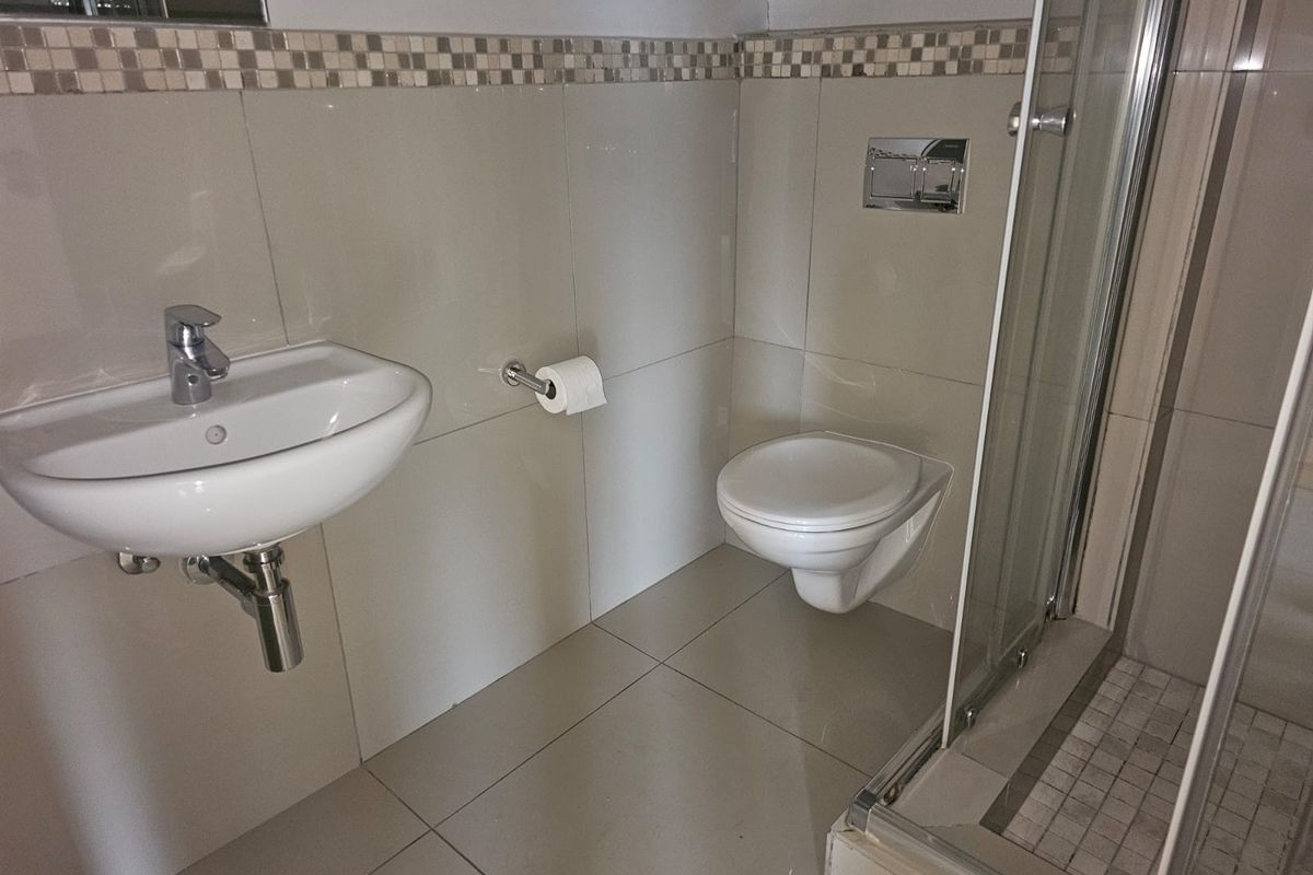A modern bathroom featuring a wall-mounted basin, wall-hung toilet with concealed cistern, and a glass-enclosed shower with tiled finishes.