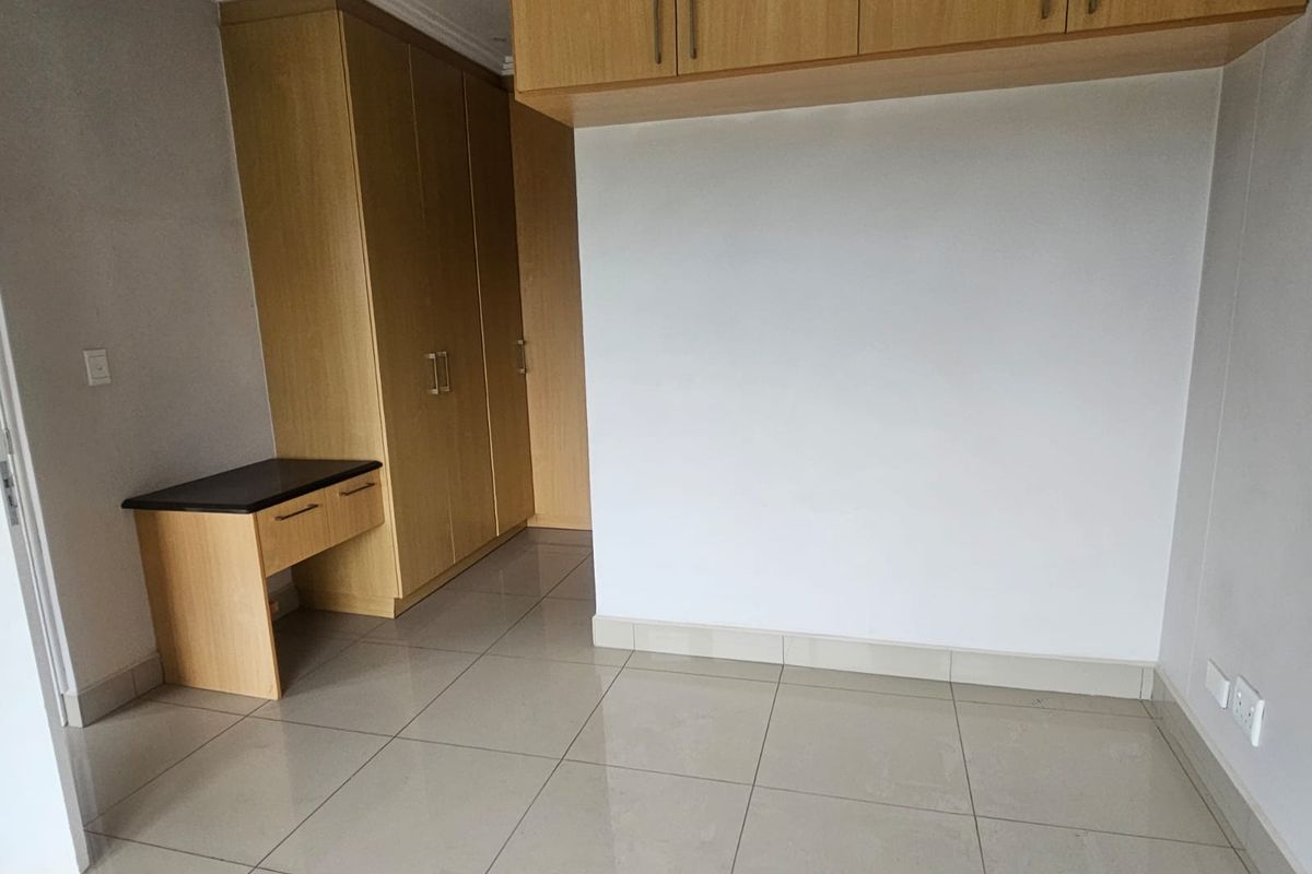 A clean, empty bedroom featuring neutral tiled flooring, extensive built-in wooden cabinetry, and a matching integrated desk area.