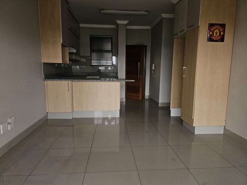 An open-plan kitchen area featuring light wood cabinetry, granite countertops, and neutral ceramic floor tiles in a well-maintained apartment setting.