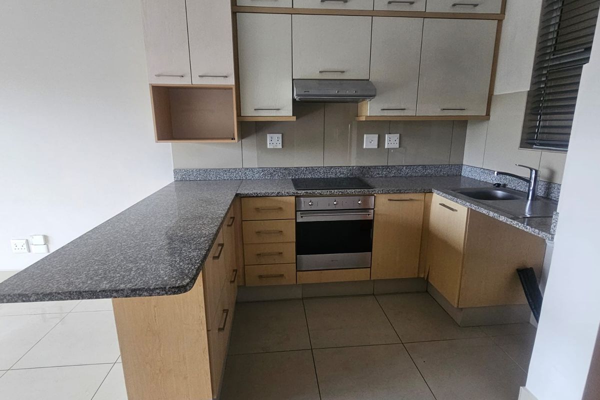 A clean, functional kitchen featuring granite countertops, built-in cabinetry, an integrated oven and hob, and tiled flooring.