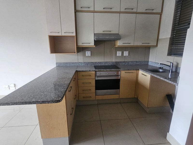A clean, functional kitchen featuring granite countertops, built-in cabinetry, an integrated oven and hob, and tiled flooring.