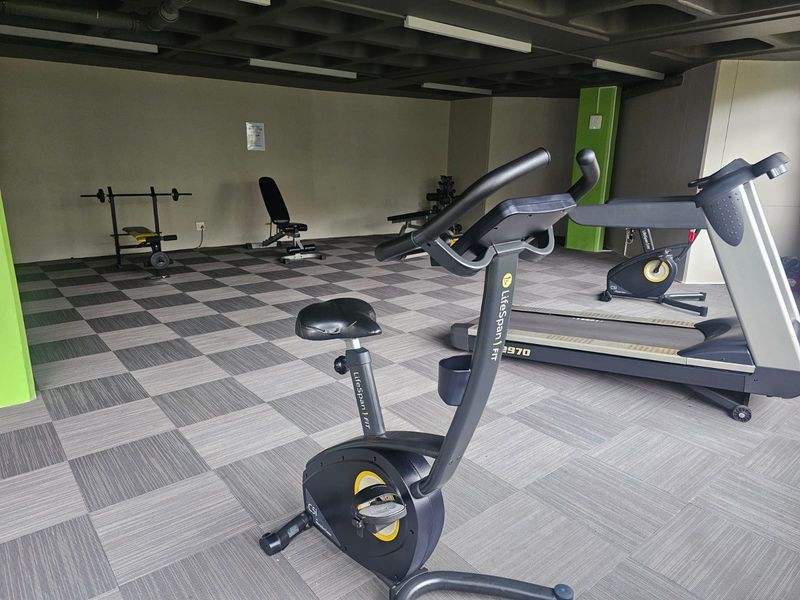 A functional apartment gym facility featuring a waffle slab ceiling and durable carpet tile flooring, equipped with various exercise machines.