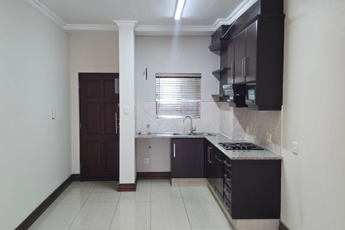 A clean, functional kitchen featuring dark wood cabinetry, granite countertops, built-in appliances, and neutral tiled flooring.