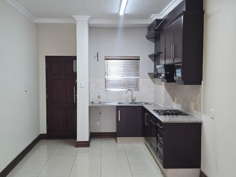 A clean, functional kitchen featuring dark wood cabinetry, granite countertops, built-in appliances, and neutral tiled flooring.