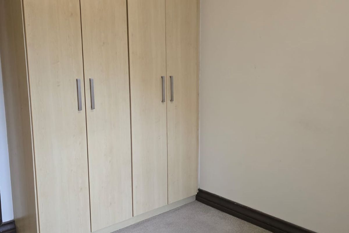 A clean, empty bedroom featuring light wood-finish built-in cupboards and neutral wall tones, providing a versatile space ready for personalization.