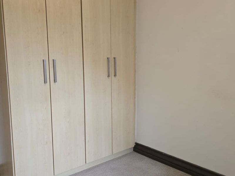 A clean, empty bedroom featuring light wood-finish built-in cupboards and neutral wall tones, providing a versatile space ready for personalization.