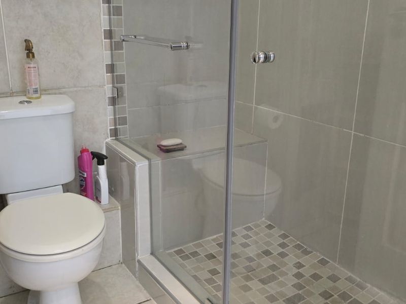 A functional bathroom featuring a glass-enclosed shower with mosaic floor tiling and neutral ceramic wall tiles.
