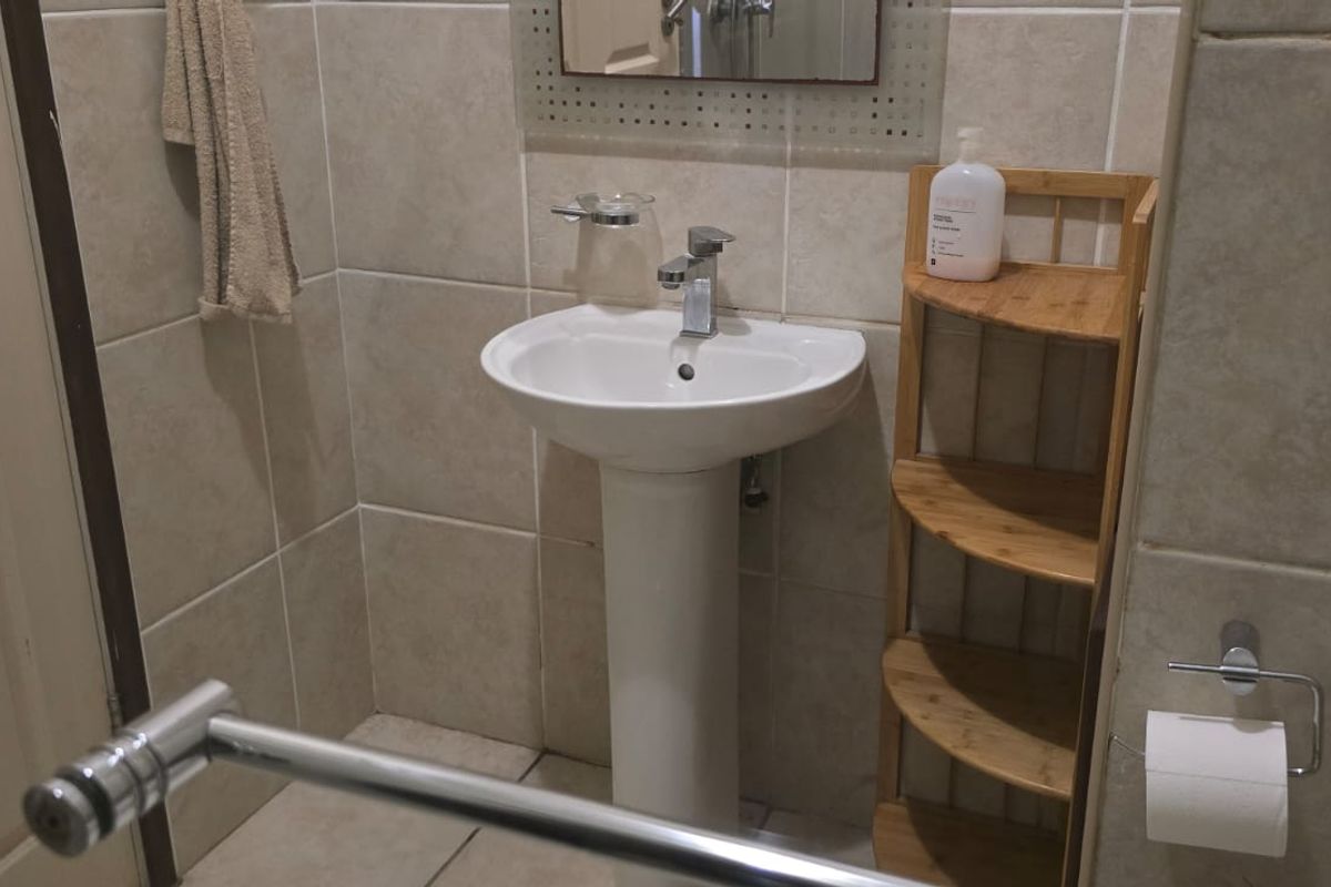 A functional bathroom featuring a pedestal basin with chrome mixer tap, tiled walls and flooring, and essential bathroom fixtures.