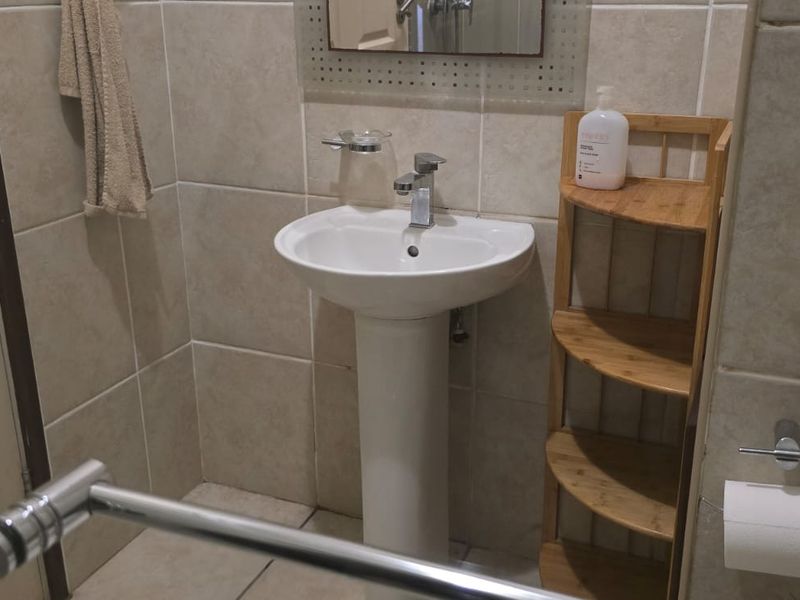 A functional bathroom featuring a pedestal basin with chrome mixer tap, tiled walls and flooring, and essential bathroom fixtures.