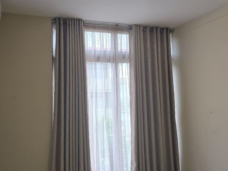 A bright, empty bedroom featuring a full-height window with curtains and a wall-mounted split-system air conditioning unit.