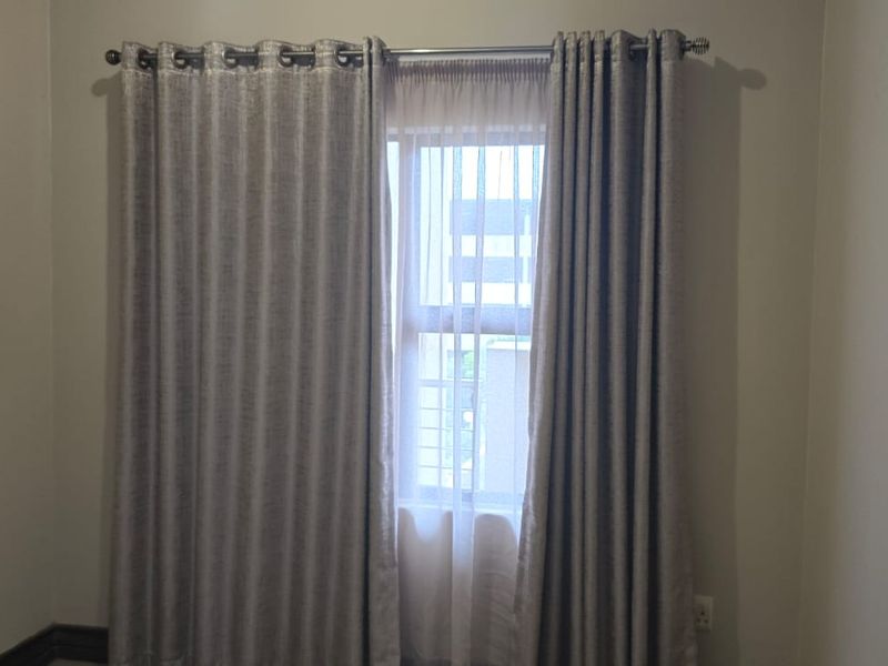A simple, neutral-toned bedroom featuring a window with installed curtain rods and curtains, providing a clean and blank canvas for interior design.