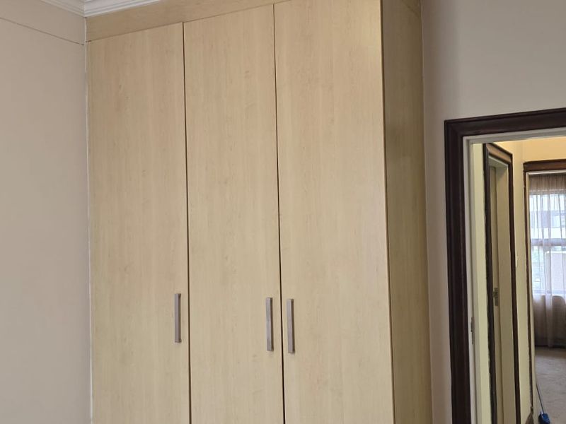 A bedroom featuring a light wood-finish built-in wardrobe and a doorway leading to an adjacent room.