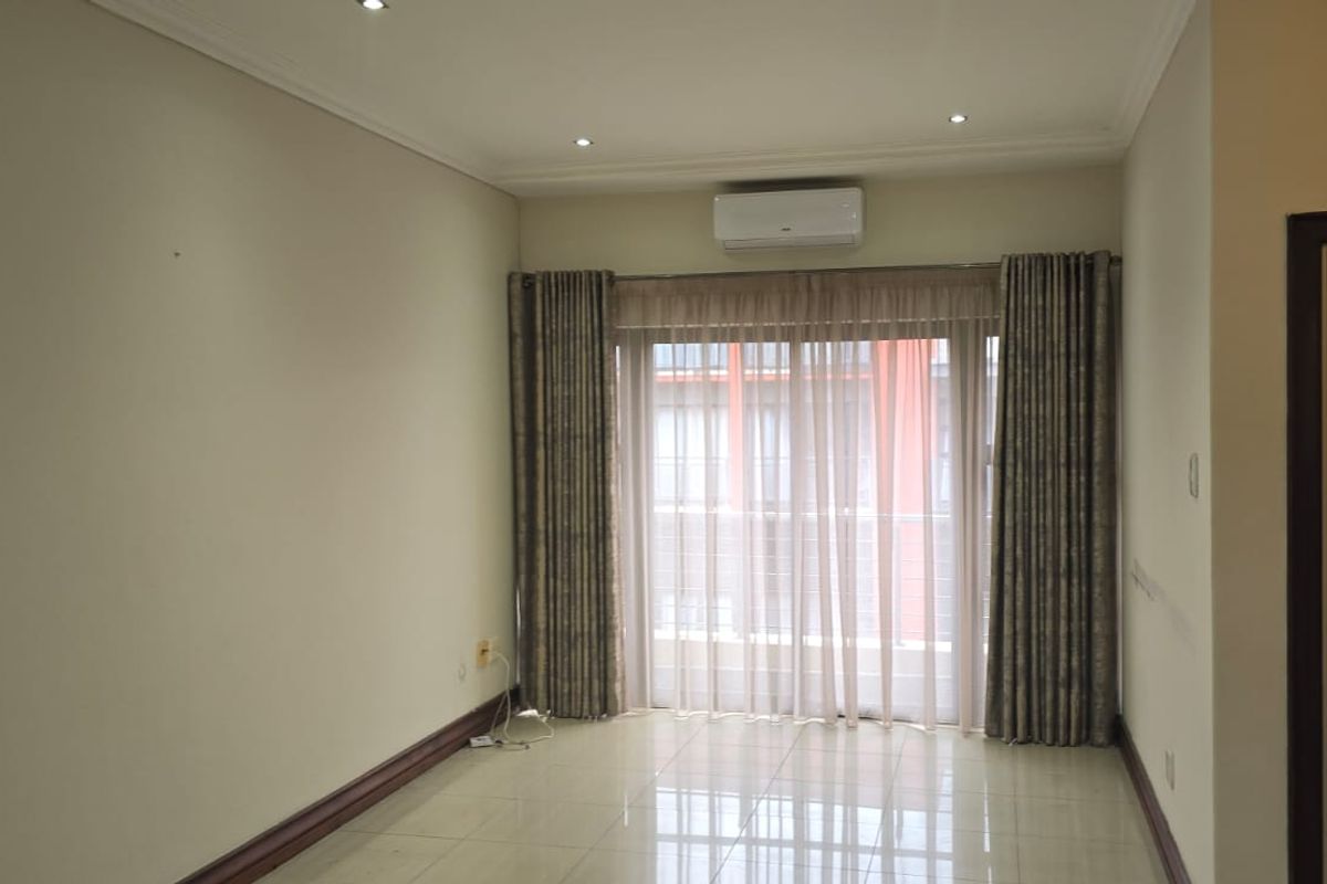 A bright, empty living room featuring tiled flooring, recessed downlights, an air conditioning unit, and a sliding glass door leading to a balcony.