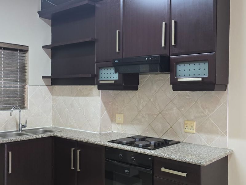 A functional kitchen featuring dark wood cabinetry, granite countertops, a built-in oven with hob, and a tiled backsplash.