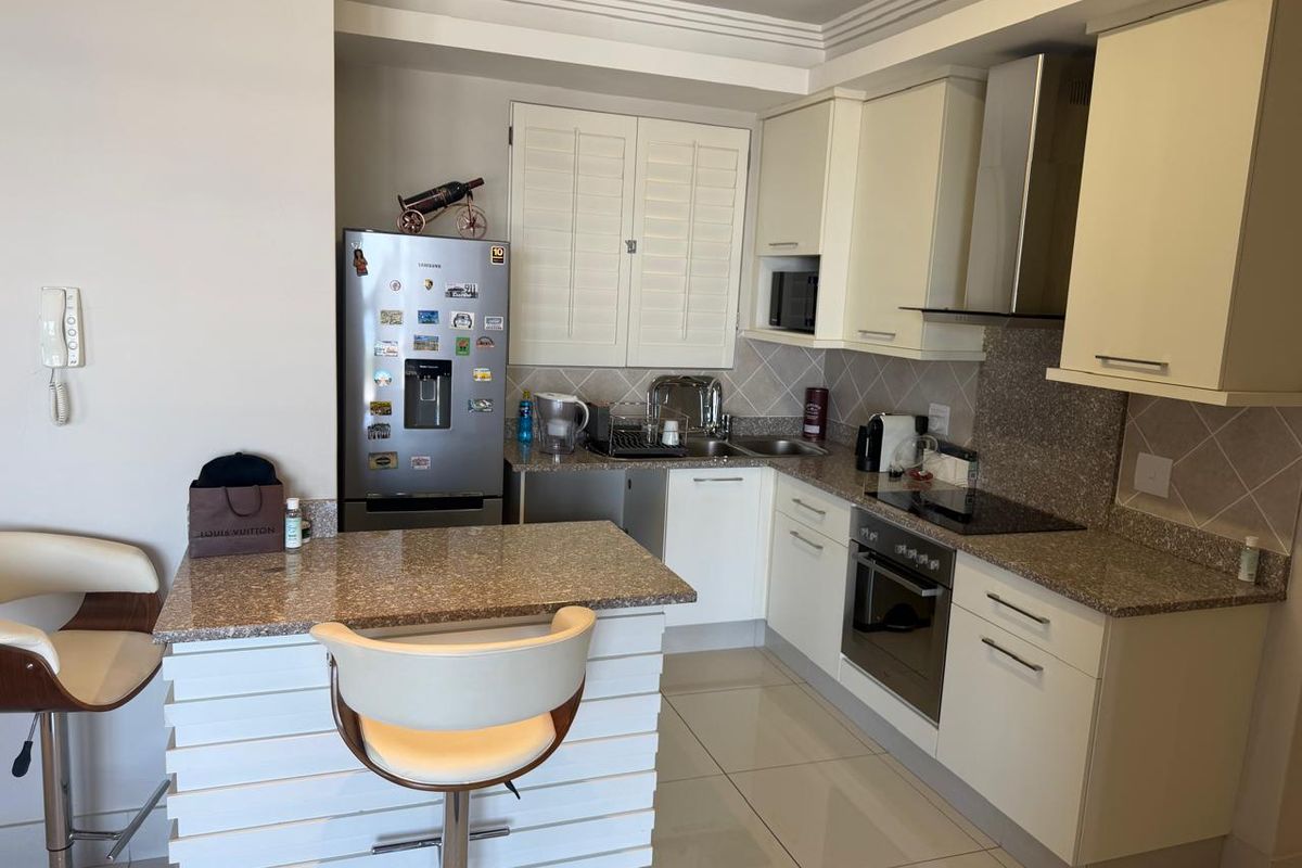 A functional kitchen featuring cream cabinetry, granite countertops, integrated appliances, and a breakfast bar, finished with tiled flooring and a neutral backsplash.