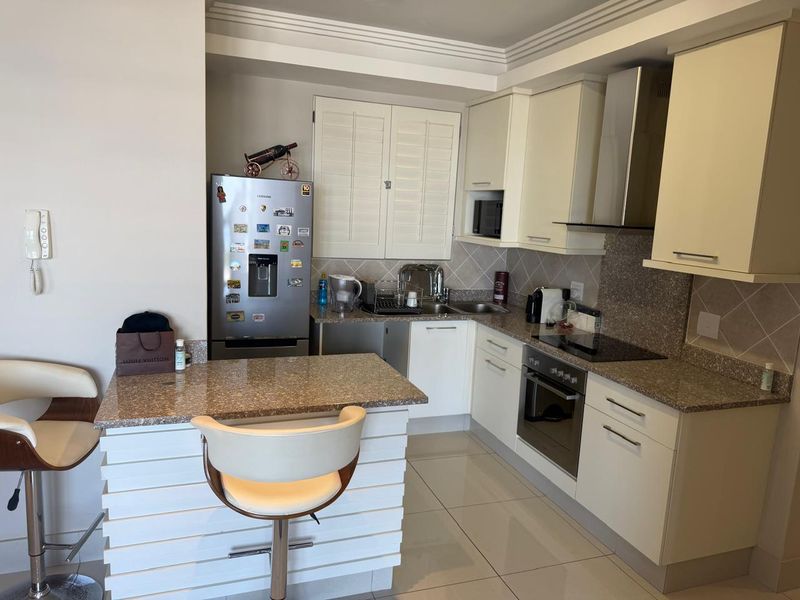 A functional kitchen featuring cream cabinetry, granite countertops, integrated appliances, and a breakfast bar, finished with tiled flooring and a neutral backsplash.