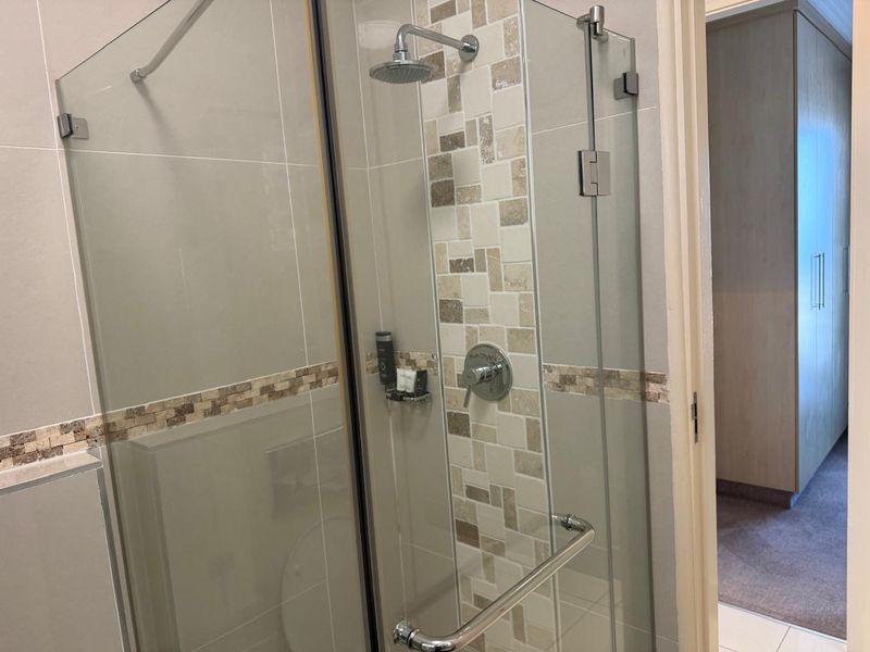 Modern bathroom featuring a glass-enclosed shower with a rainfall shower head and decorative mosaic tile accents.