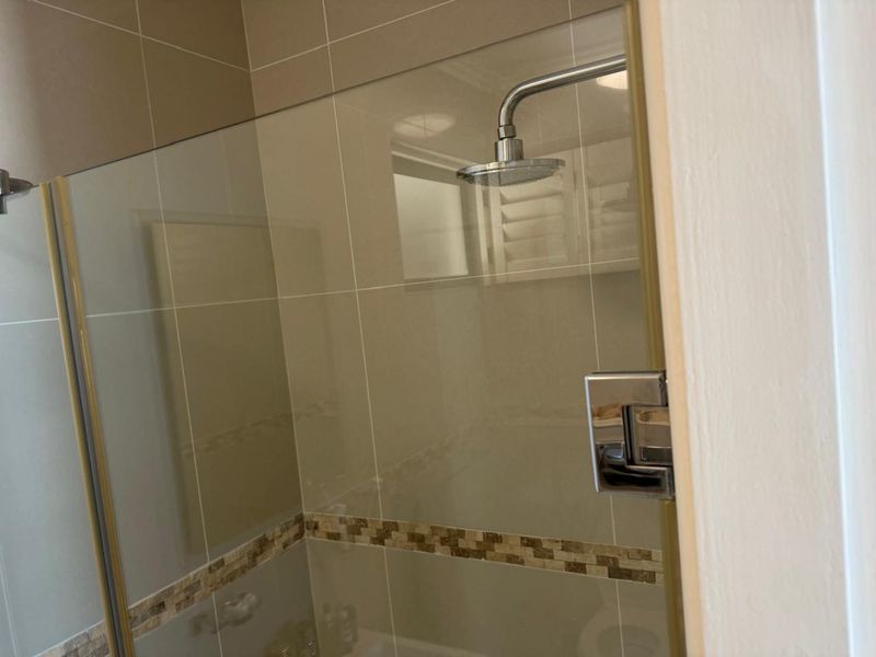 A modern bathroom shower enclosure featuring a glass screen, rain shower head, and neutral-toned wall tiles with a decorative mosaic border.