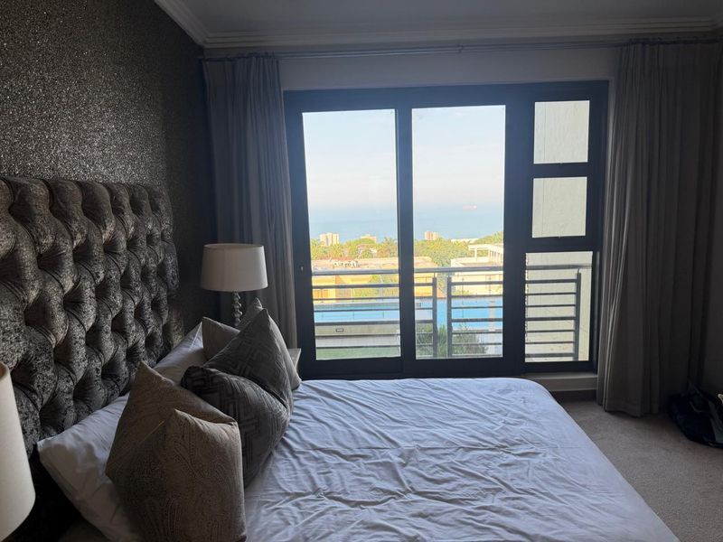 Spacious bedroom featuring large sliding glass doors that open onto a balcony with scenic coastal and pool views.