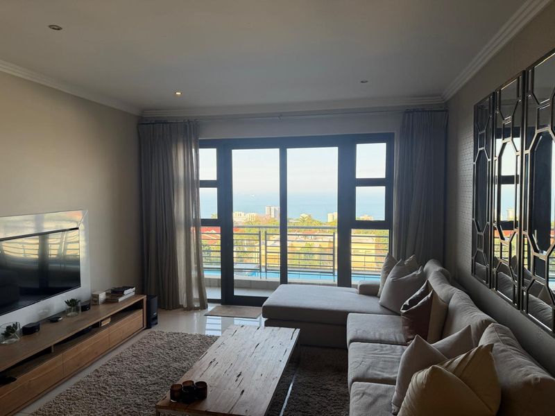 A well-maintained living room featuring tiled floors, recessed lighting, and large sliding glass doors that open to a balcony with ocean views.