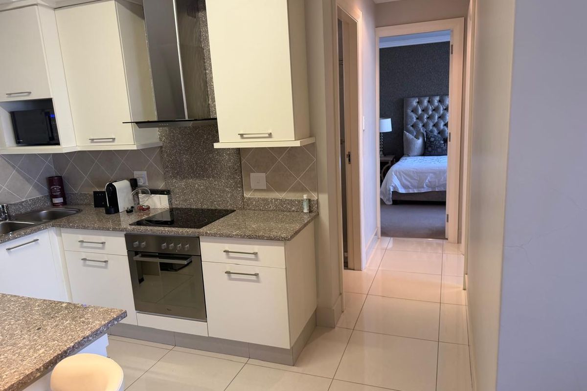 Modern kitchen featuring granite countertops, built-in oven, electric hob, and tiled flooring, with a view leading into the adjacent bedroom.