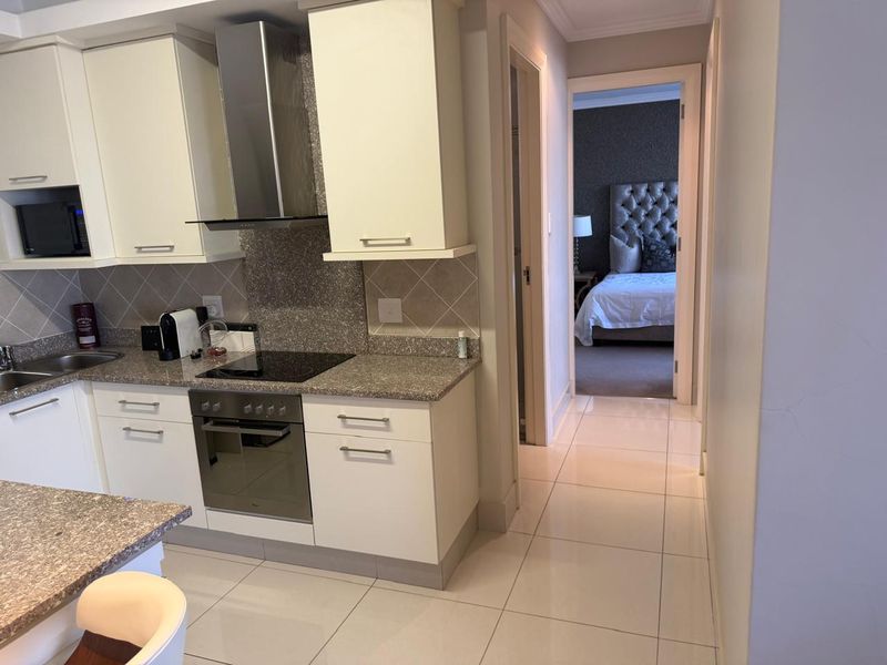 Modern kitchen featuring granite countertops, built-in oven, electric hob, and tiled flooring, with a view leading into the adjacent bedroom.