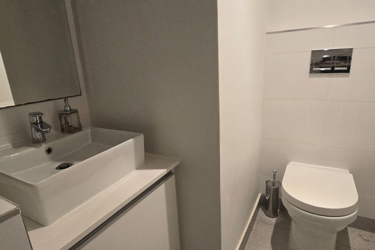 A modern bathroom featuring a wall-mounted toilet with a chrome flush plate, a vessel sink set on a vanity cabinet, and a wall mirror.