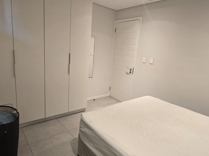 A clean bedroom featuring neutral tiled flooring and ample built-in cupboard storage space.