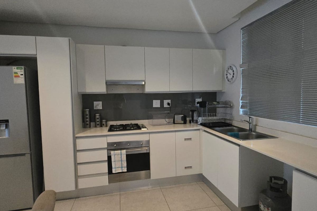 Modern kitchen featuring white cabinetry, stone countertops, integrated gas hob, electric oven, and stainless steel sink with natural light from the window.