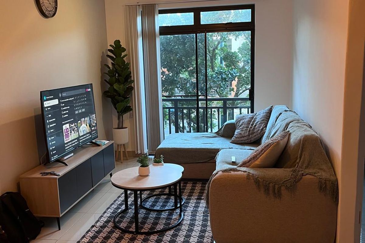A well-maintained living room featuring large format floor tiles, modern lighting, and a sliding glass door providing access to a balcony.