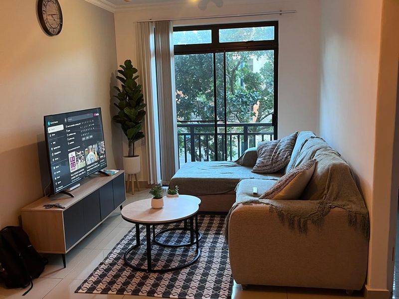 A well-maintained living room featuring large format floor tiles, modern lighting, and a sliding glass door providing access to a balcony.