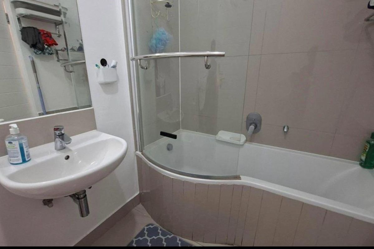 A functional bathroom featuring a wall-mounted basin, a bathtub with a glass shower screen, and tiled wall finishes.