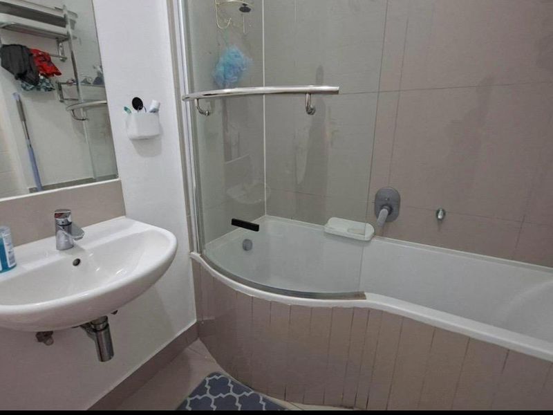 A functional bathroom featuring a wall-mounted basin, a bathtub with a glass shower screen, and tiled wall finishes.