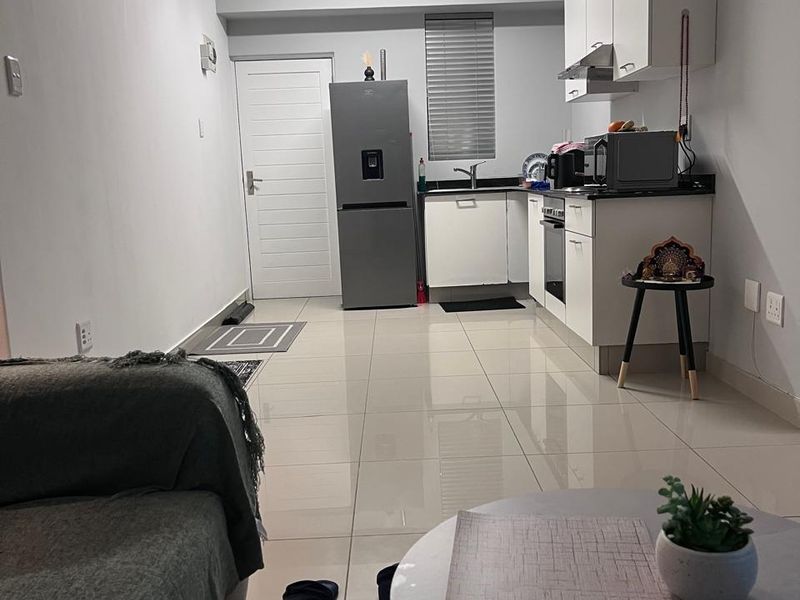 Open-plan living and kitchen area featuring tiled flooring, modern white cabinetry, built-in oven and hob, and neutral finishes throughout.