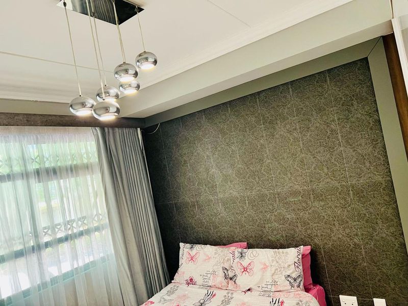 A well-maintained bedroom featuring a decorative feature wall, modern multi-pendant lighting, and a cove ceiling design.