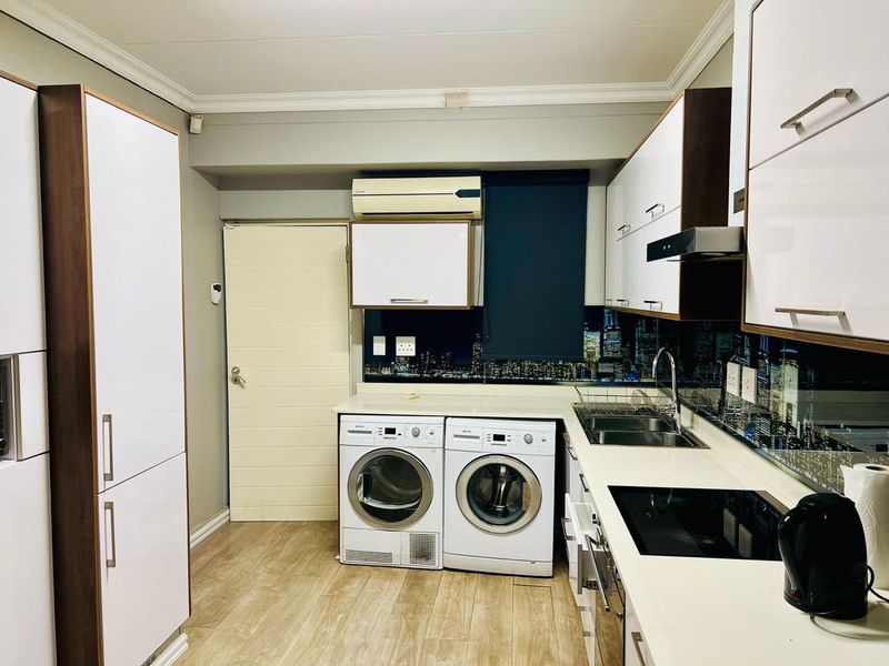Modern kitchen featuring white cabinetry, integrated appliances, electric hob, extractor fan, and a unique city-scape splashback, providing a functional and stylish workspace.