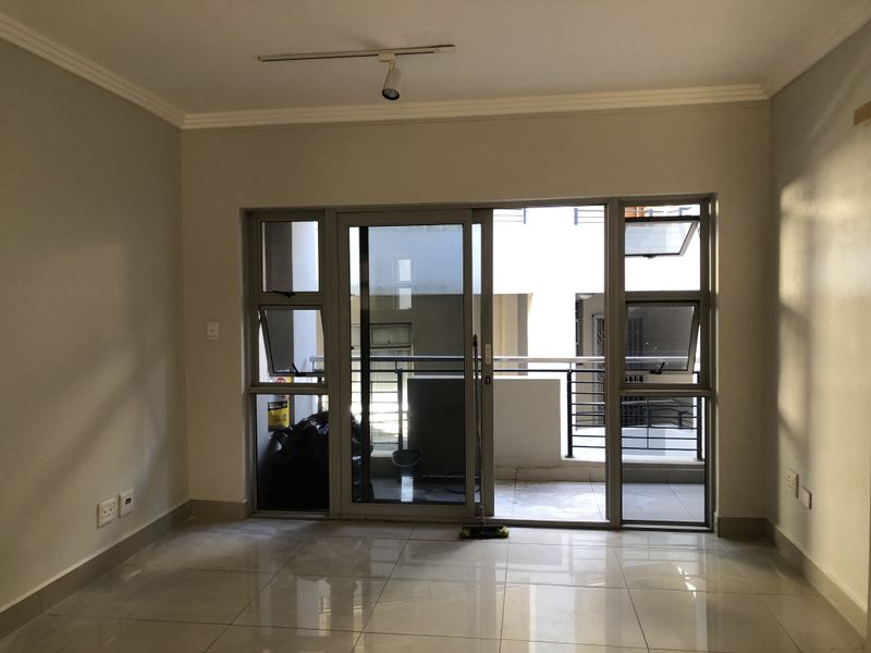 An empty living room featuring polished tile flooring, track lighting, and a large sliding glass door providing access to a balcony.